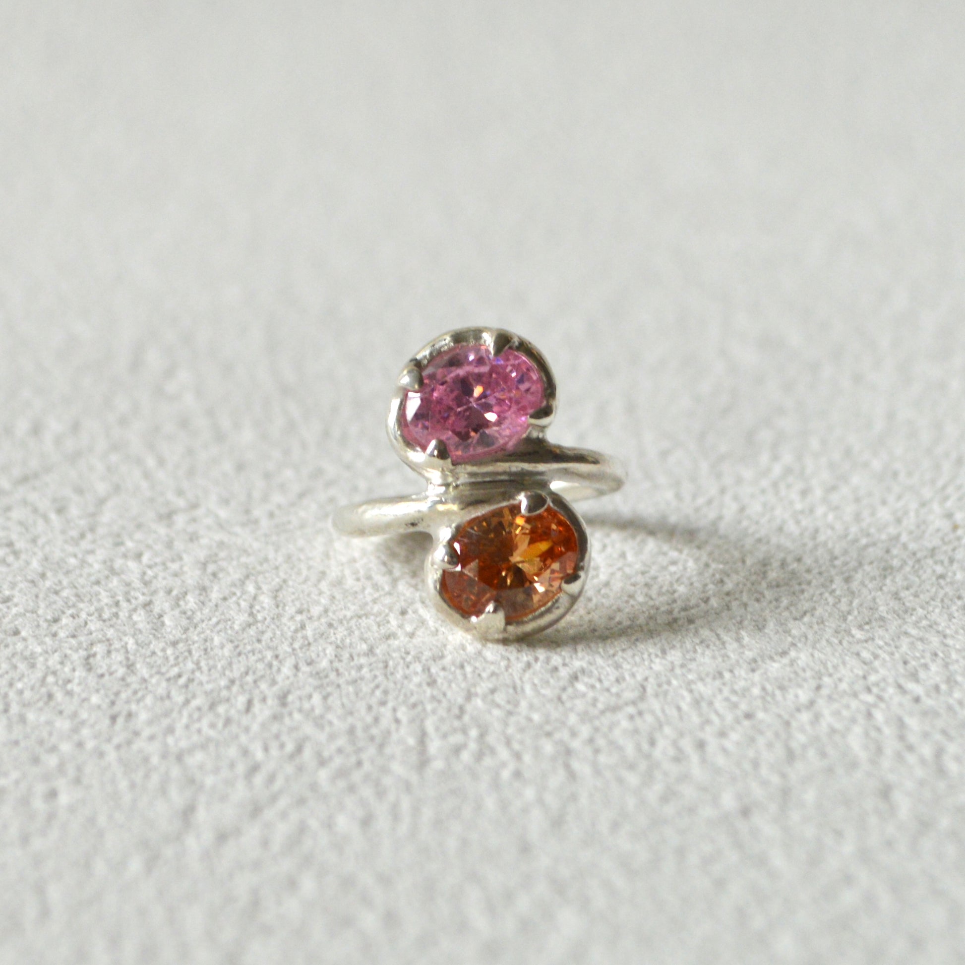 Silver ring with pink and orange gemstones on a light gray background