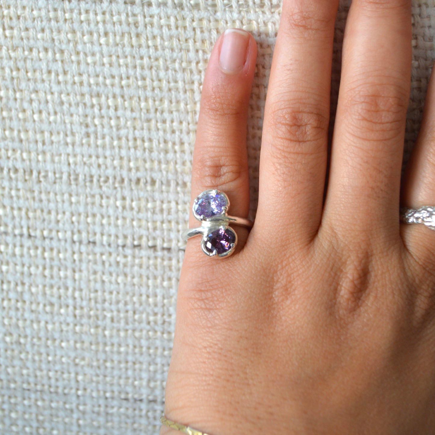Hand wearing a silver ring with purple gemstones on a textured fabric background